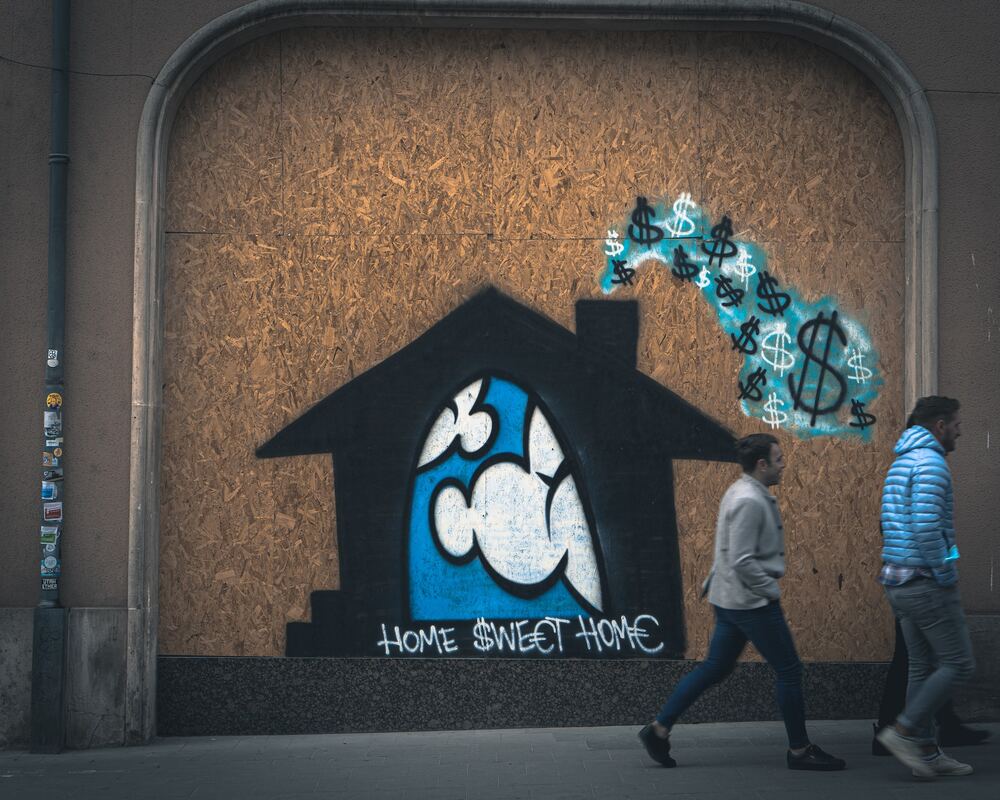 A graffiti of a home with dollar-shaped smoke clouds coming out of its chimney.