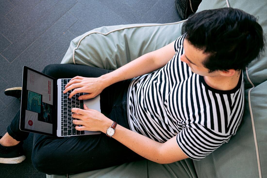 A man doing something on his laptop while sitting on a sofa. Picture