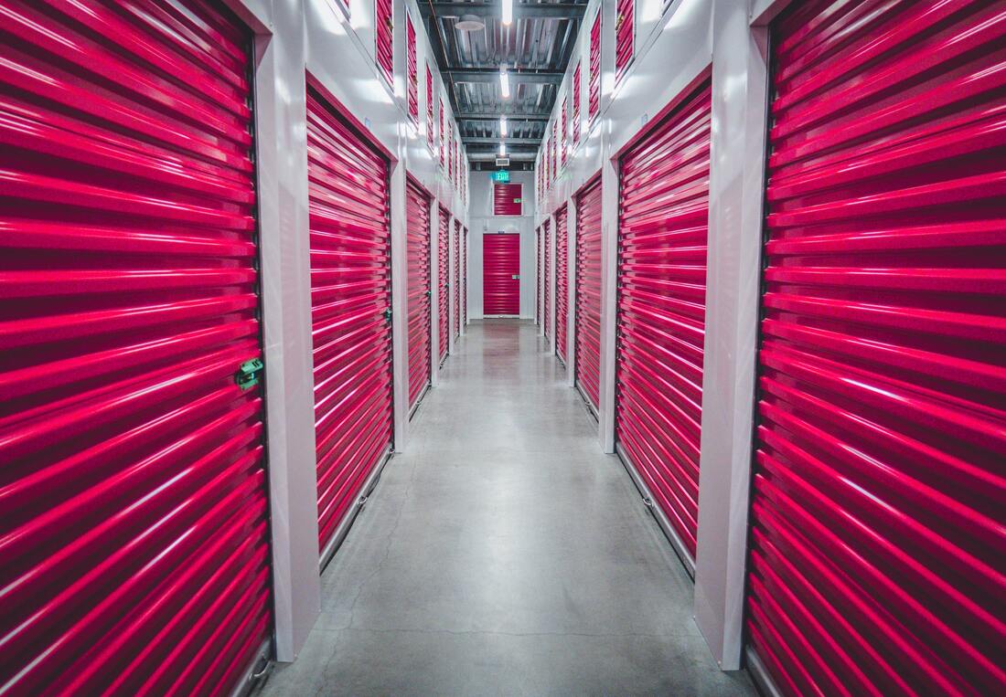A self-storage facility's corridor with pink roll-up doors on either side.