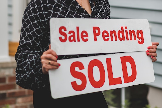 A person holding signs “Sale pending” and “Sold.”