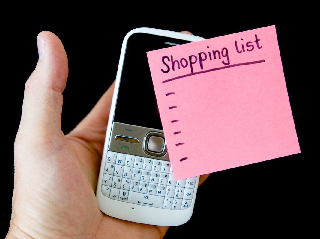 A person holding a phone with a pink post-it note with shopping list written on it