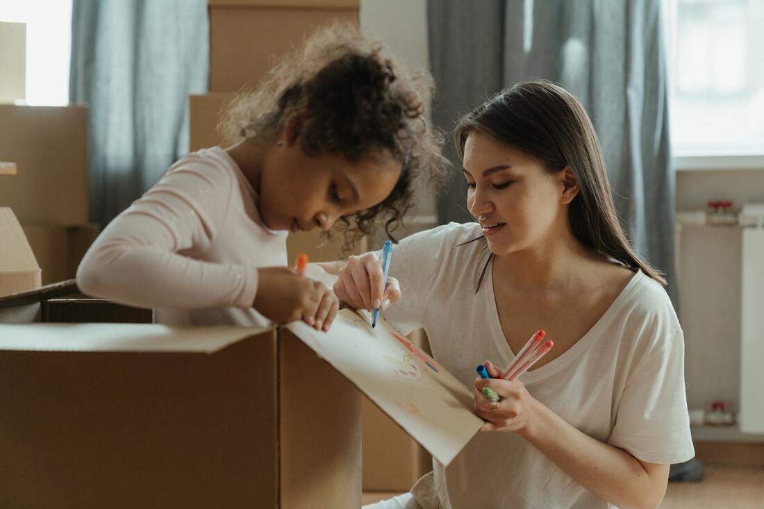A woman and her daughter drawing on moving boxes after buying a home for a growing family.